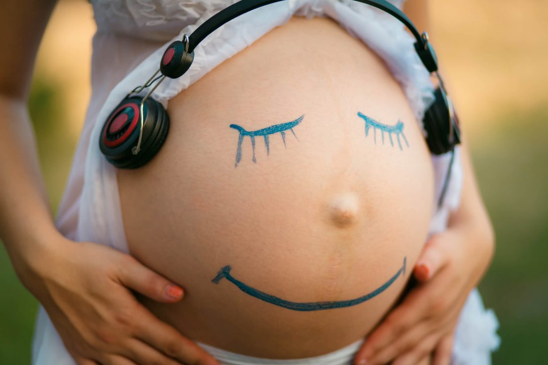 Ventre dénudé de femme enceinte sur lequel est dessiné un visage souriant, en bleu