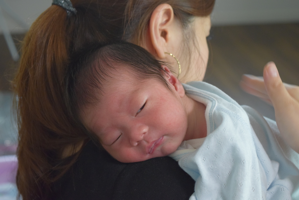 Un adulte qui tient un bébé en position verticale contre son épaule pendant le rot.