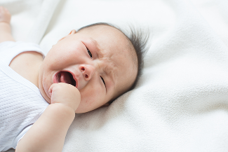 baby crying with their hand reaching for their mouth