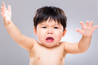 A baby crying and reaching their arms up.