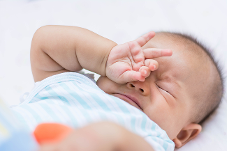 A baby with their head down and their hands over their eyes and nose