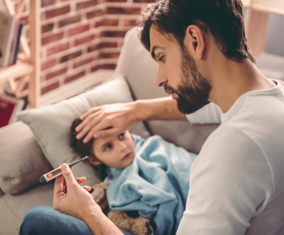Un adulte regarde un thermomètre avec sa main sur le front d'un enfant