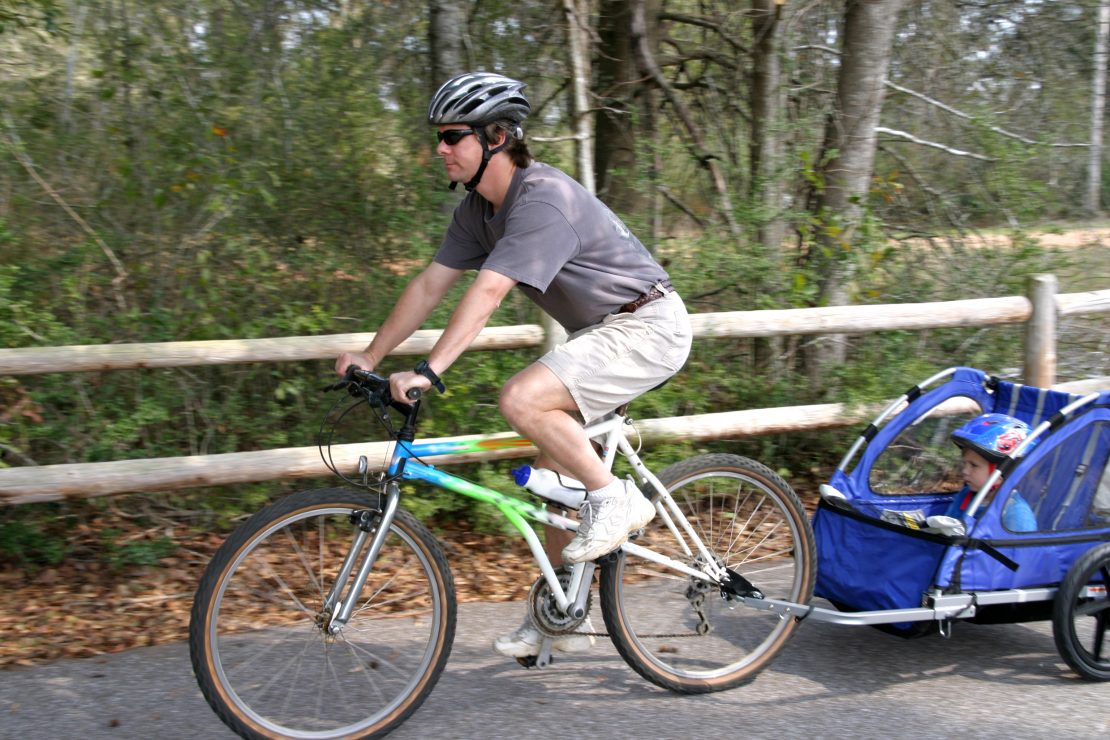 an adult riding a bike with a blue trailer connected at the back