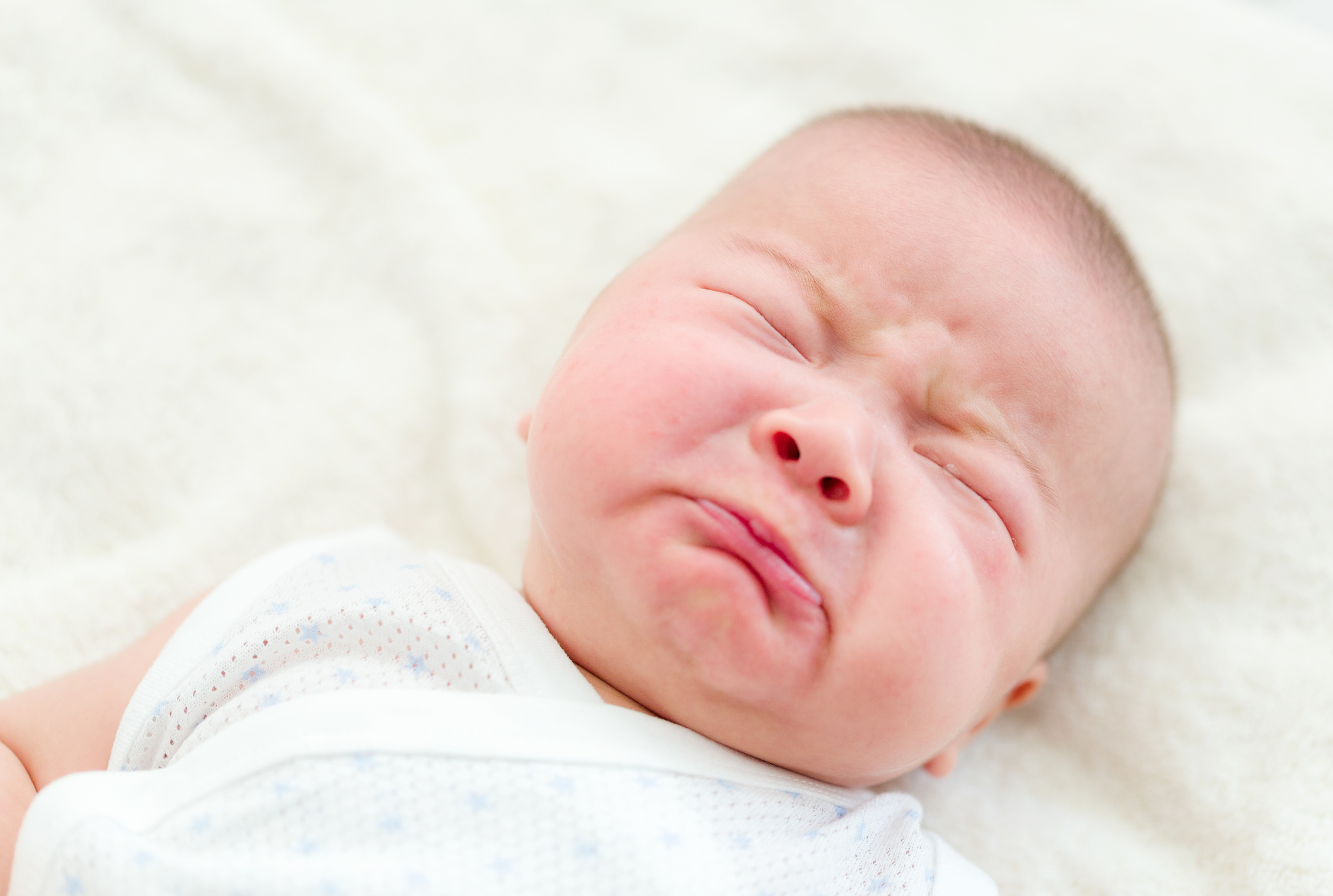 A baby with closed eyes and a sad expression.