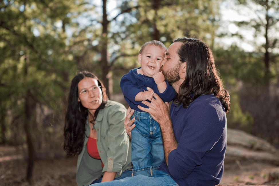 Father kissing baby boy, mother sitting in the background.