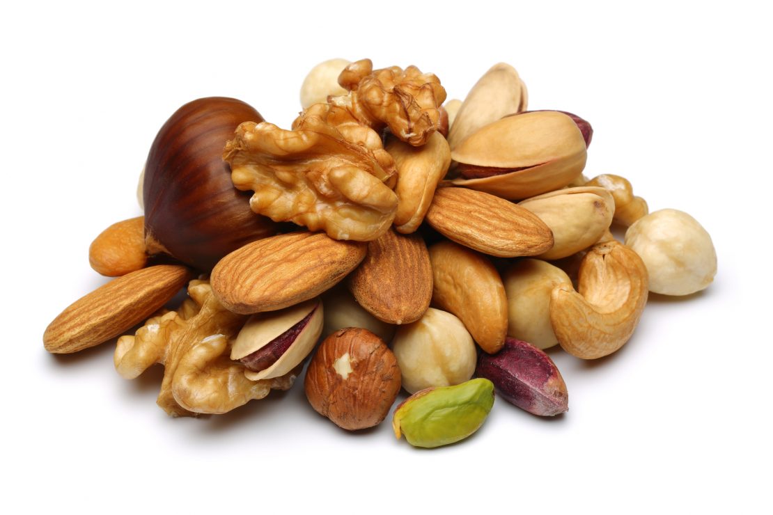 Une pile de noix contenant des amandes, des noix de Grenoble, des noisettes et des pistaches sur une surface blanche.