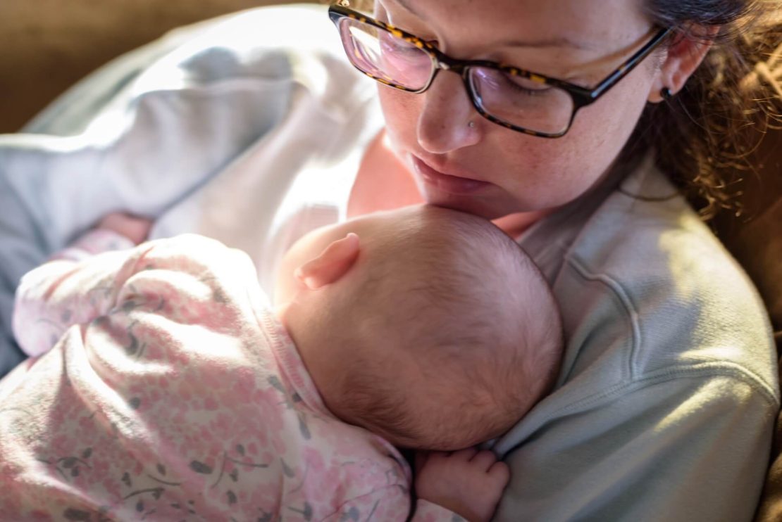 Personne tenant un bébé qui repose sur sa poitrine. Le bébé porte une tenue rose montrant des motifs floraux