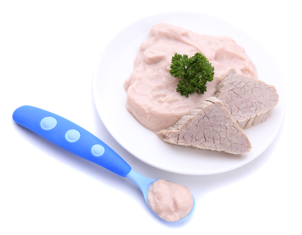 Un rôti en purée dans une assiette blanche avec deux petites tranches de rôti et du persil sur le dessus. Il y a une cuillère pour bébé bleue avec de la purée de viande.