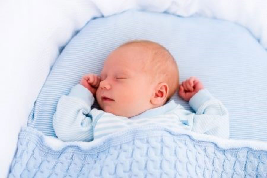 Un bébé couché sur le dos avec une couverture qui le couvre jusqu’aux aisselles et qui est rentrée dans les côtés du berceau