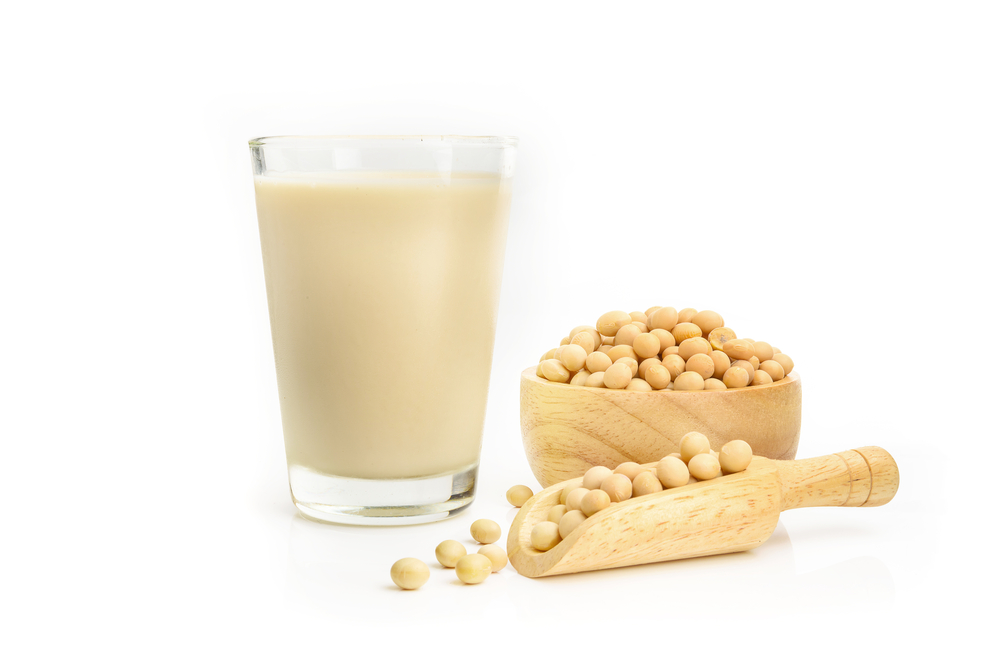 Un verre de lait de soya à côté d’un petit bol et d’une petite cuillère remplis de fèves de soya